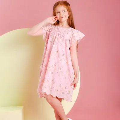 Menina ruiva com vestido rosa de bordado vazado, mangas em babado e barra recortada, em fundo rosa com arco amarelo