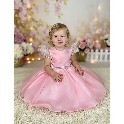 Menina pequena sentada usando vestido rosa acetinado com abas de tule nos ombros, cinto de pérolas e saia rodada