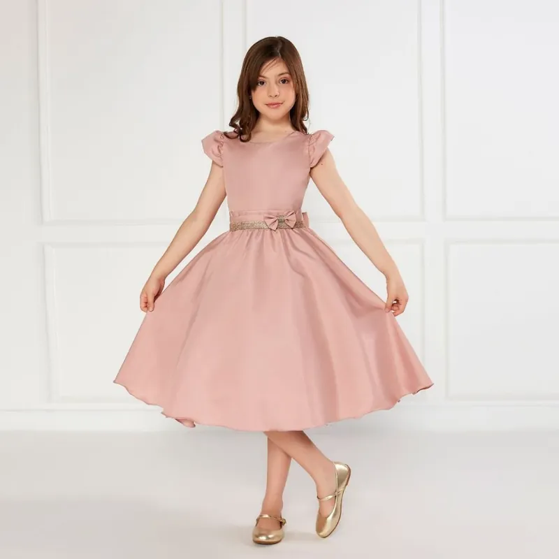 Menina de vestido rosê com manguinha franzida, cinto de strass dourado com laço e saia rodada, de sapatilha dourada