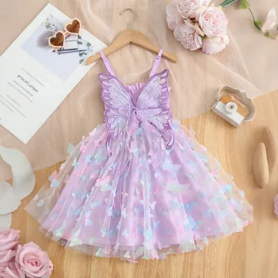 Vestido infantil lilás de tule com borboletas coloridas aplicadas e asas no busto, pendurado em cabide de madeira