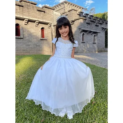 Menina sorrindo com vestido longo branco rendado e saia de tule, de tiara, no gramado em frente a um castelo de pedra