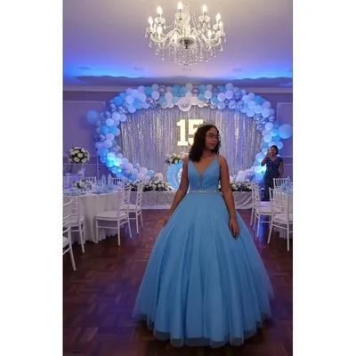 Debutante com vestido longo azul-claro de saia ampla e cinto brilhante em salão decorado para festa de 15 anos