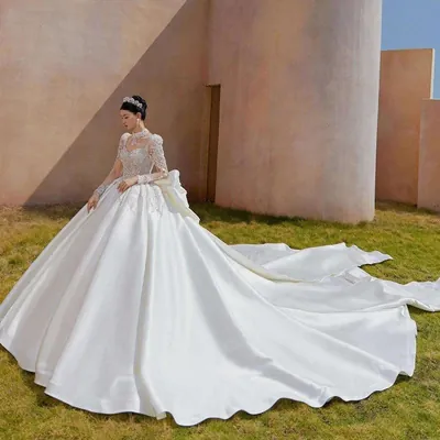 Noiva sobre gramado com vestido de corpo bordado, gola alta, mangas longas transparentes e saia lisa com cauda longa