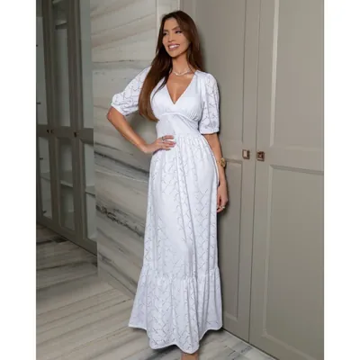 Mulher com vestido branco longo de laise, decote em V, mangas bufantes e babado na barra, em closet de portas cinza
