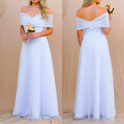 Modelo de frente e de costas com vestido branco longo ombro a ombro, tecido de bolinhas e buquê de rosas claras
