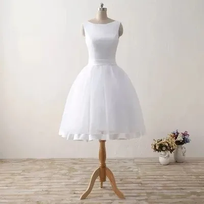 Vestido de noiva branco curto em manequim, corpo liso sem mangas, decote canoa, faixa na cintura e saia rodada de tule