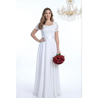 Noiva sorrindo com vestido branco longo, mangas curtas de renda, decote coração, faixa na cintura e buquê de rosas vermelhas