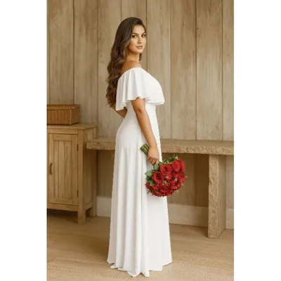Noiva de perfil em vestido longo branco ombro a ombro com babado, segurando buquê de rosas vermelhas