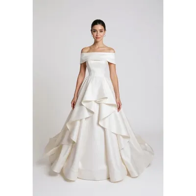 Noiva com vestido off-white ombro a ombro, corpo estruturado e saia ampla com babados em cascata e pequena cauda
