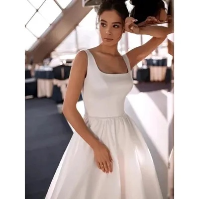 Noiva em salão envidraçado com vestido branco liso de decote quadrado, alças largas e saia ampla franzida