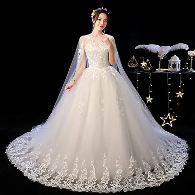 Noiva com vestido branco de saia ampla, renda no corpo, capa de tule nos ombros e barrado rendado com cauda