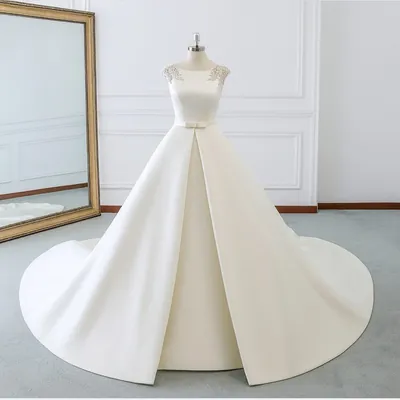 Vestido de noiva em cetim marfim no manequim, com bordado nos ombros, laço na cintura e cauda longa espalhada