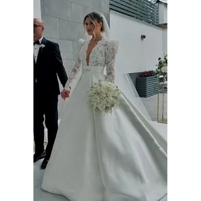 Noiva com vestido de renda de manga longa, decote em V, saia ampla lisa, véu longo e buquê branco