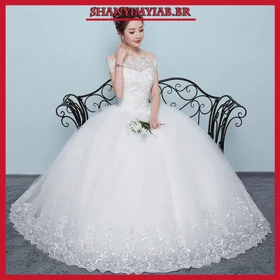 Noiva com vestido branco de baile, decote ombro a ombro de renda e saia de tule armada com barra bordada, segurando buquê