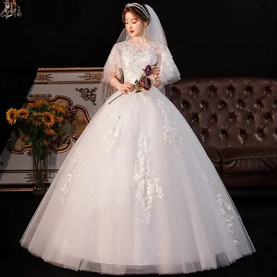Noiva com vestido branco de saia ampla de tule, mangas esvoaçantes e aplicações de folhas, segurando rosas marsala