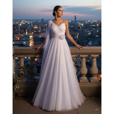 Mulher em terraço à noite com vestido branco longo rodado de tule, decote em V, flor na cintura e faixa de tule no ombro
