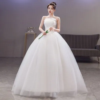 Noiva com vestido branco tomara que caia, busto franzido e saia de tule muito volumosa, segurando copos-de-leite
