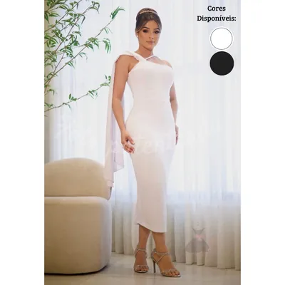 Mulher com vestido tubinho midi branco justo, decote assimétrico e capa de tecido caindo de um dos ombros, em sala clara