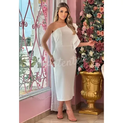 Mulher com vestido tubinho midi branco de um ombro só e babado lateral, em loja rosa com painel de rosas
